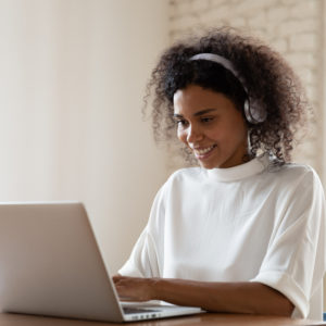 Black woman wearing headphones while working on a laptop.